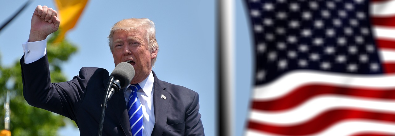 Donald Trump egy kampányrendezvényen J.D. Vance-szel egy színpadon, amerikai zászlók előtt.